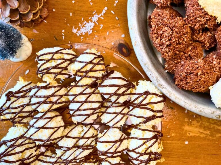 A glass plate full of chocolate drizzled coconut macaroons. There are more in a metal pie plate.