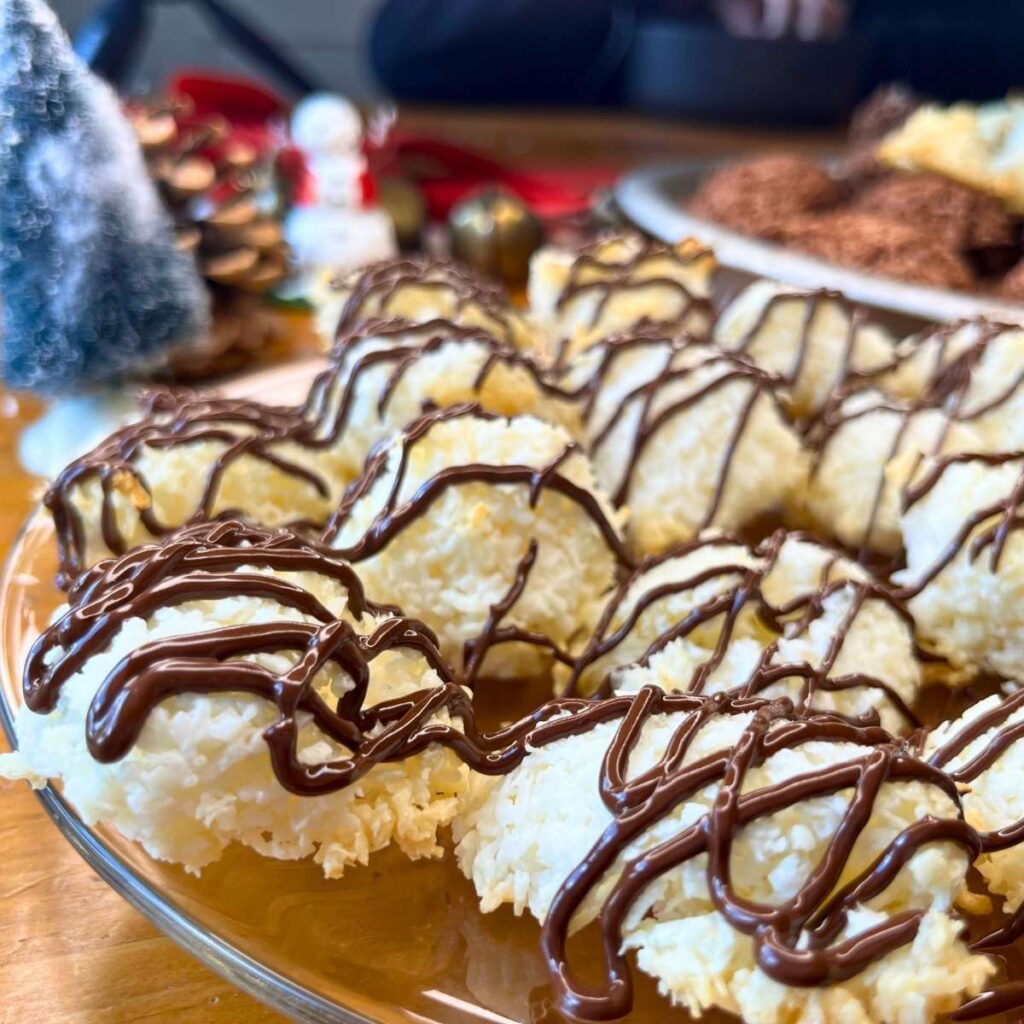 There are coconut macaroons on a glass plate drizzled with chocolate.