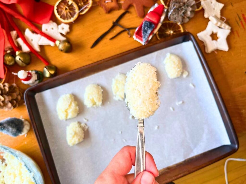 There is a woman holding a coconut mixture on a spoon. There are more on the tray in the background.