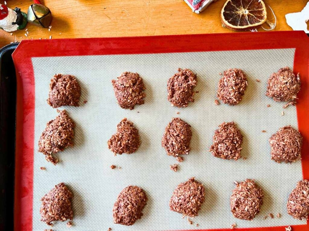 Chocolate macaroons on a lined baking sheet.