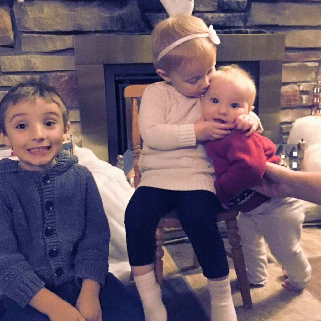 There are three small children in front of a fireplace.