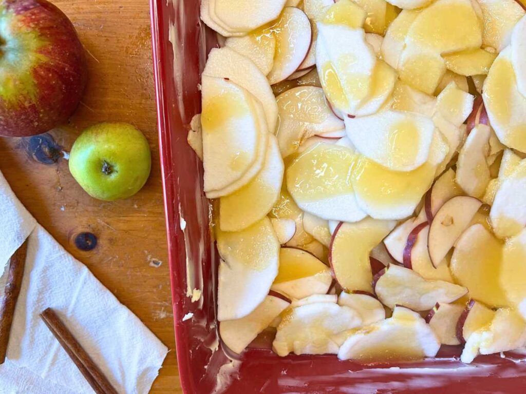 A red casserole dish with sliced apples and honey inside.