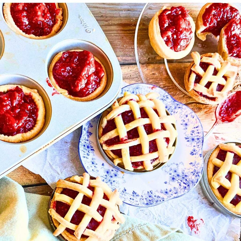 A collection of raspberry mini tarts. Some have a lattice top and some are open.