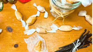 An overhead look at caramel candies wrapped in wax paper. There are more in a jar.