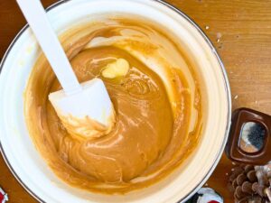 There is a woman stirring caramel with a small pad of butter inside.