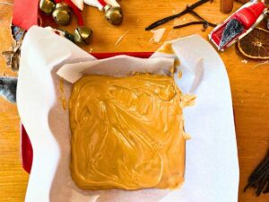 A soft caramel mixture is in a parchment paper lined square casserole dish.