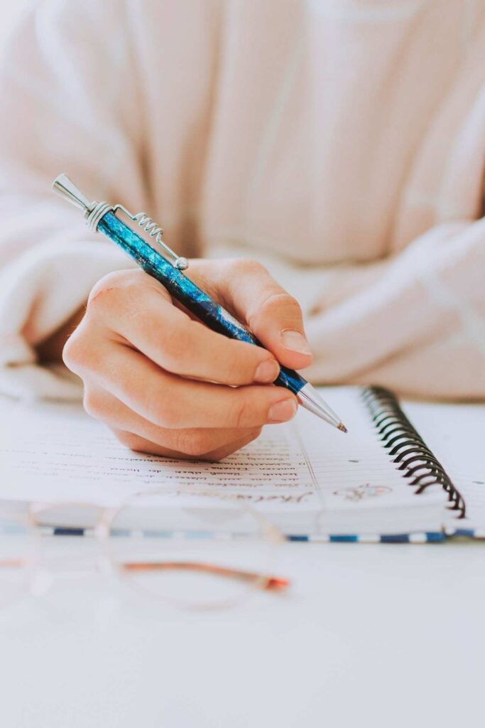 A woman is writing in a note book with a blue pen.