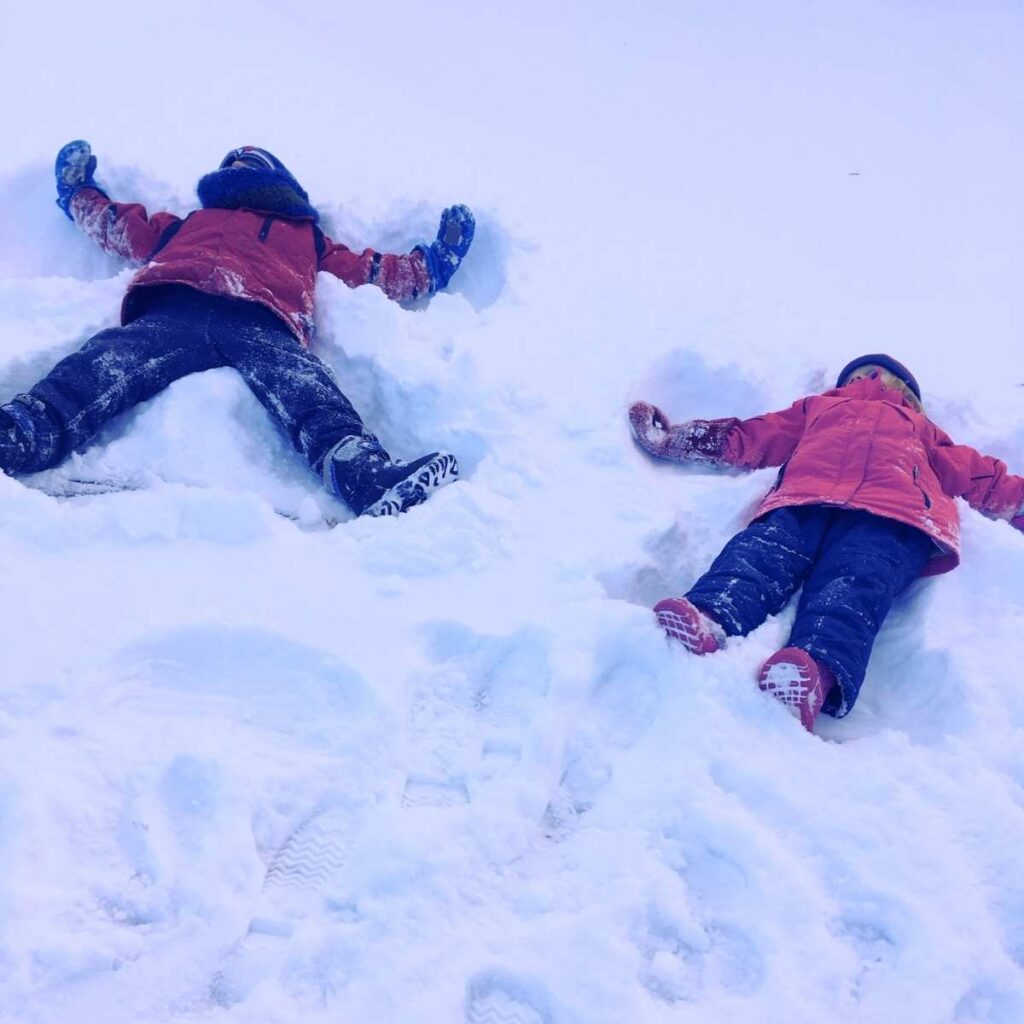 There are two children making snow angels.