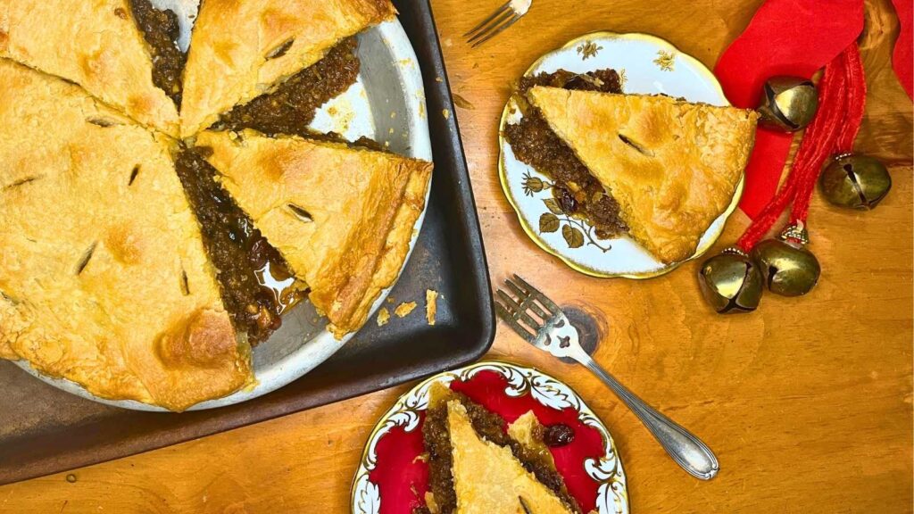 A mincemeat pie that has been sliced. Two plates have slices of pie on them.