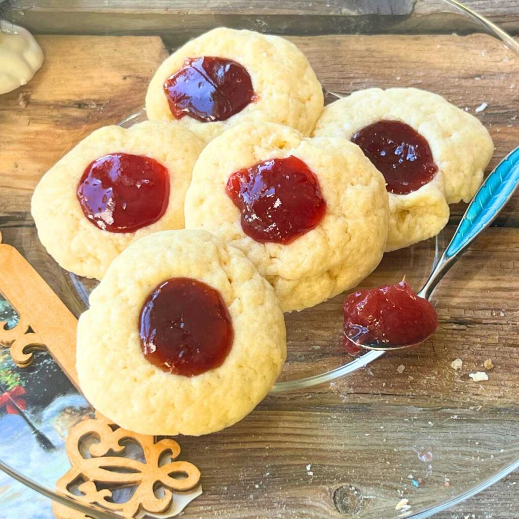 Five cookies with jam centres on a glass plate.