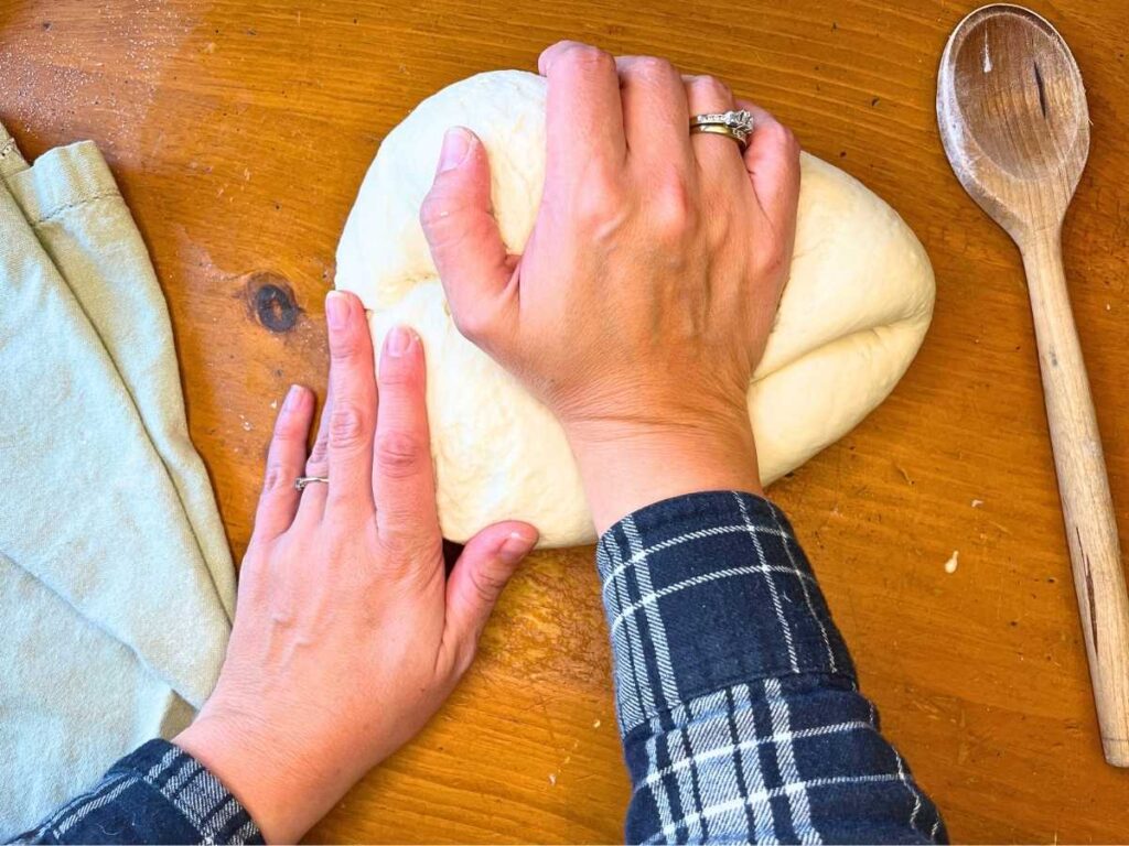 A woman kneading dough on a wooden table.