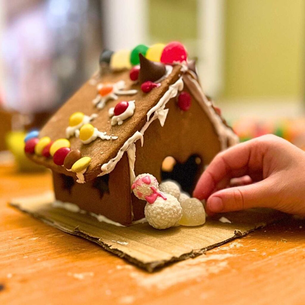 There is a child decorating a gingerbread house.