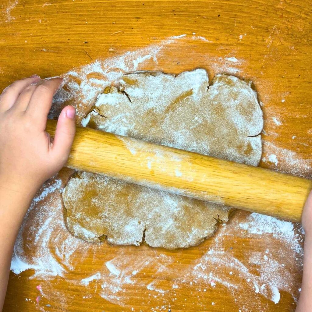 A child is rolling out gingerbread house dough with a rolling pin.