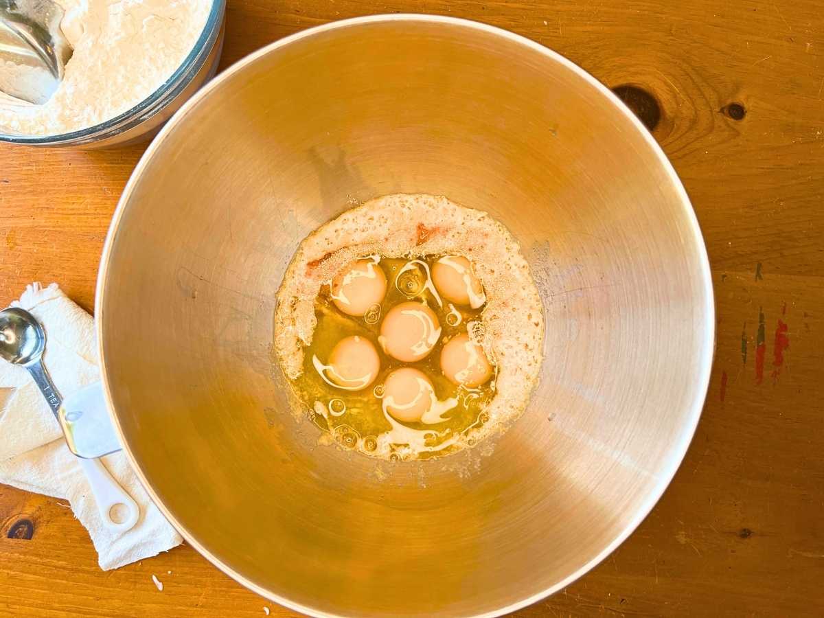 A metal bowl with yeast, water and eggs inside.