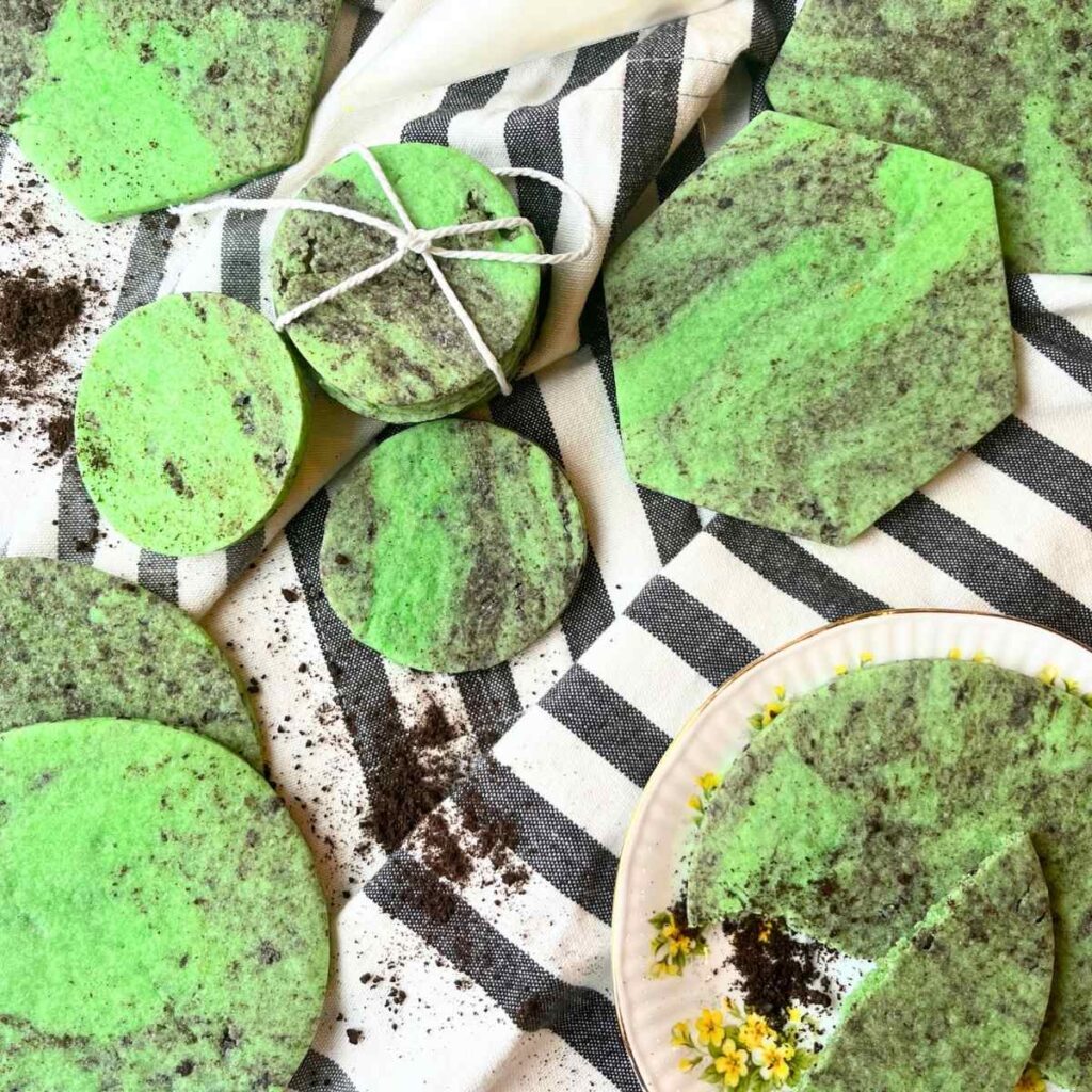 Black and green sugar cookies on a white and grey cloth.