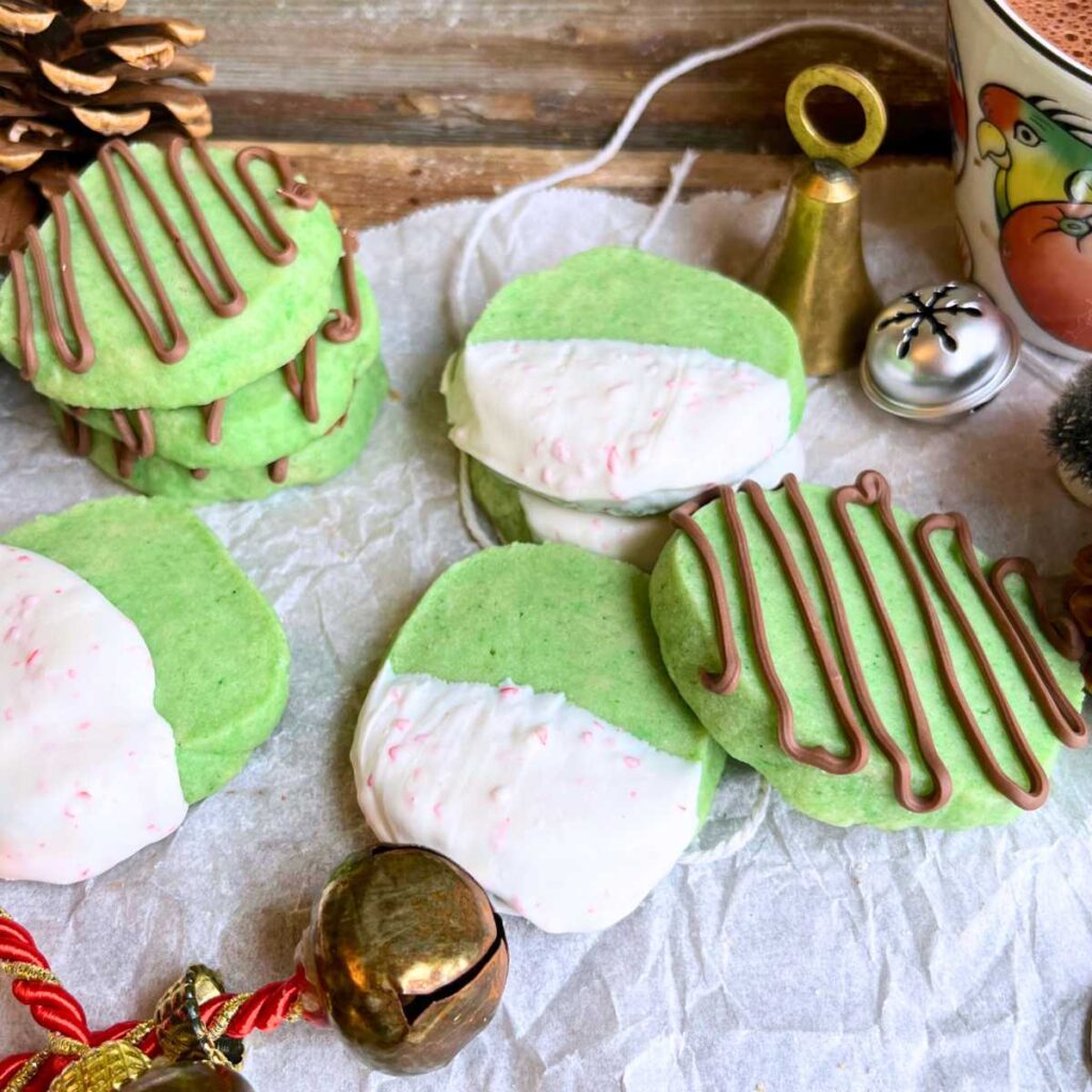 A collection of green mint shortbread cookies dipped in white chocolate and some are drizzled in chocolate.