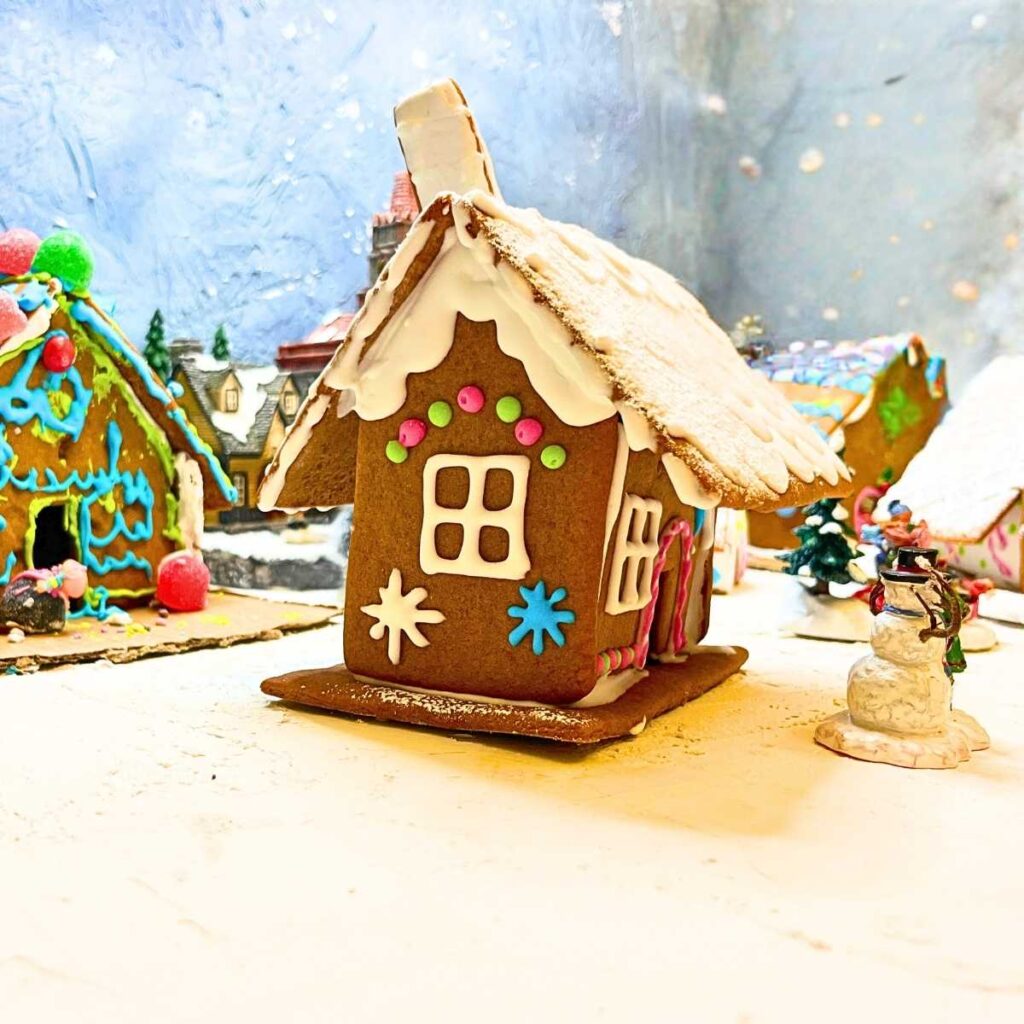 A gingerbread house decorated with royal icing. There are more houses in the background set up in a Christmas villange