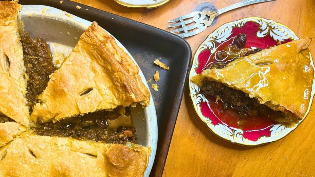 A sliced mincemeat pie with a red plate beside with a slice of the pie on it.