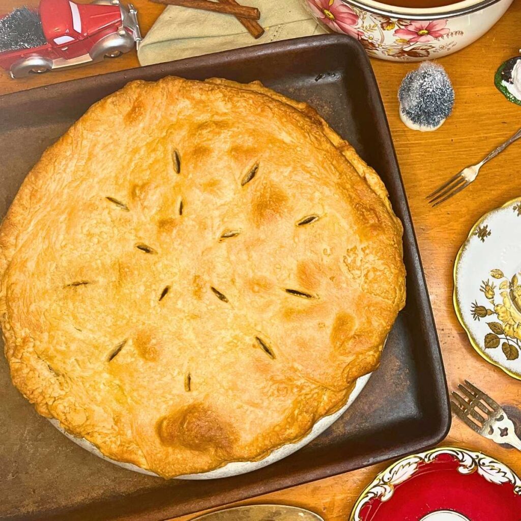 A mincemeat pie on a tray and a pot in the background. There are Christmas decorations around.