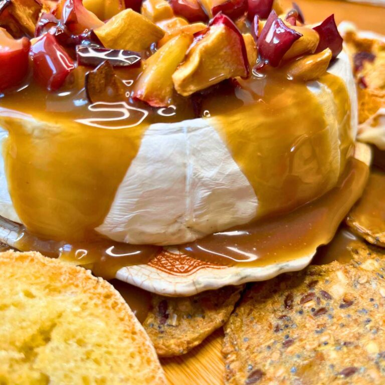 A close up look at a baked Brie covered in chopped apple and caramel.