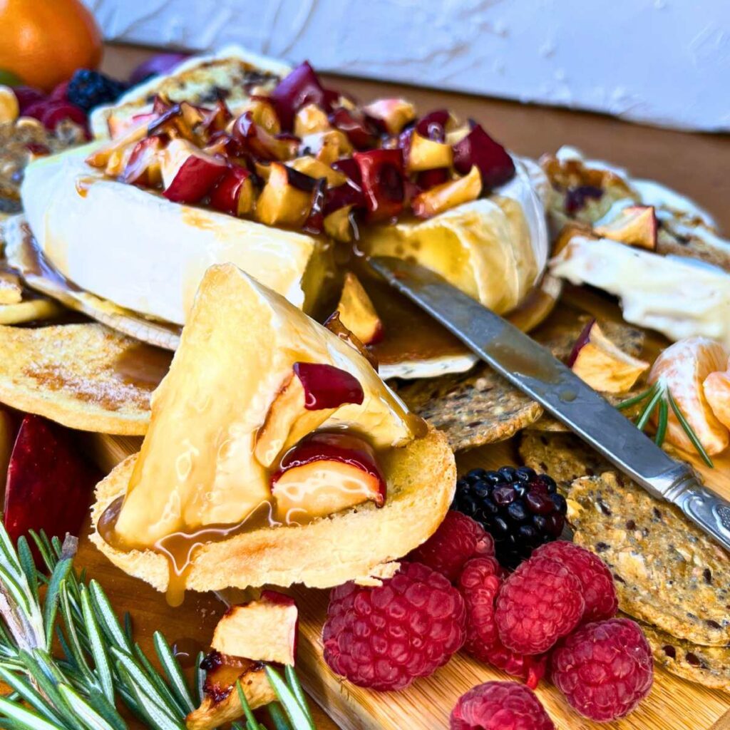 A baked Brie with apple and caramel on top. There is a slice on a piece of bread in front.