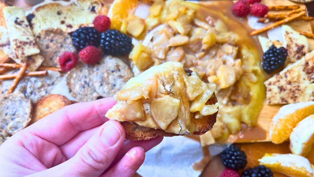 A woman holding a slice of bread with baked brie and apple caramel sauce.