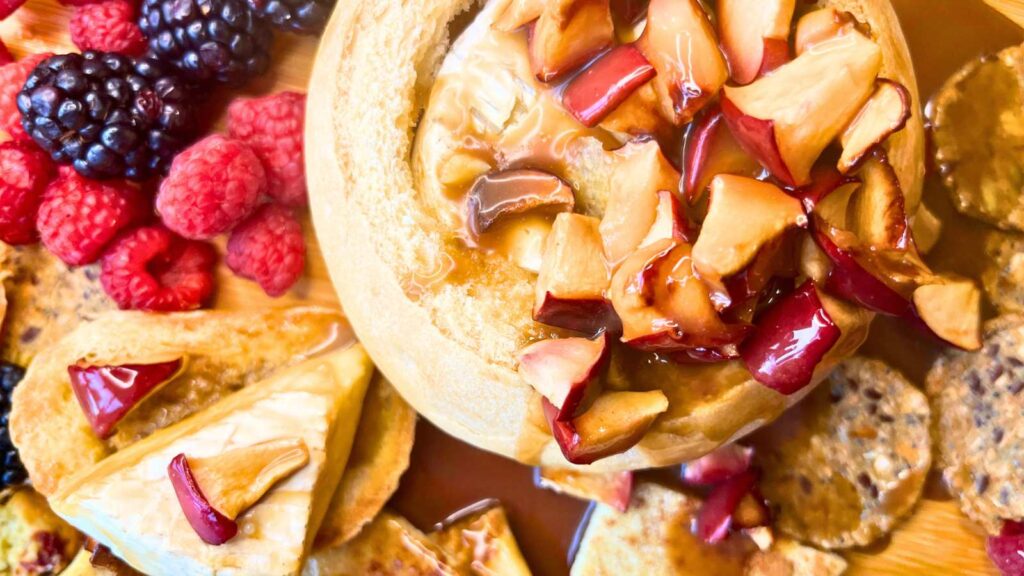 A bread bowl with a baked Brie inside. There are chopped apples and caramel on top.