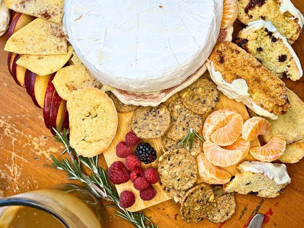 A baked Brie surrounded by crackers, bread, fresh fruit, and cookies.