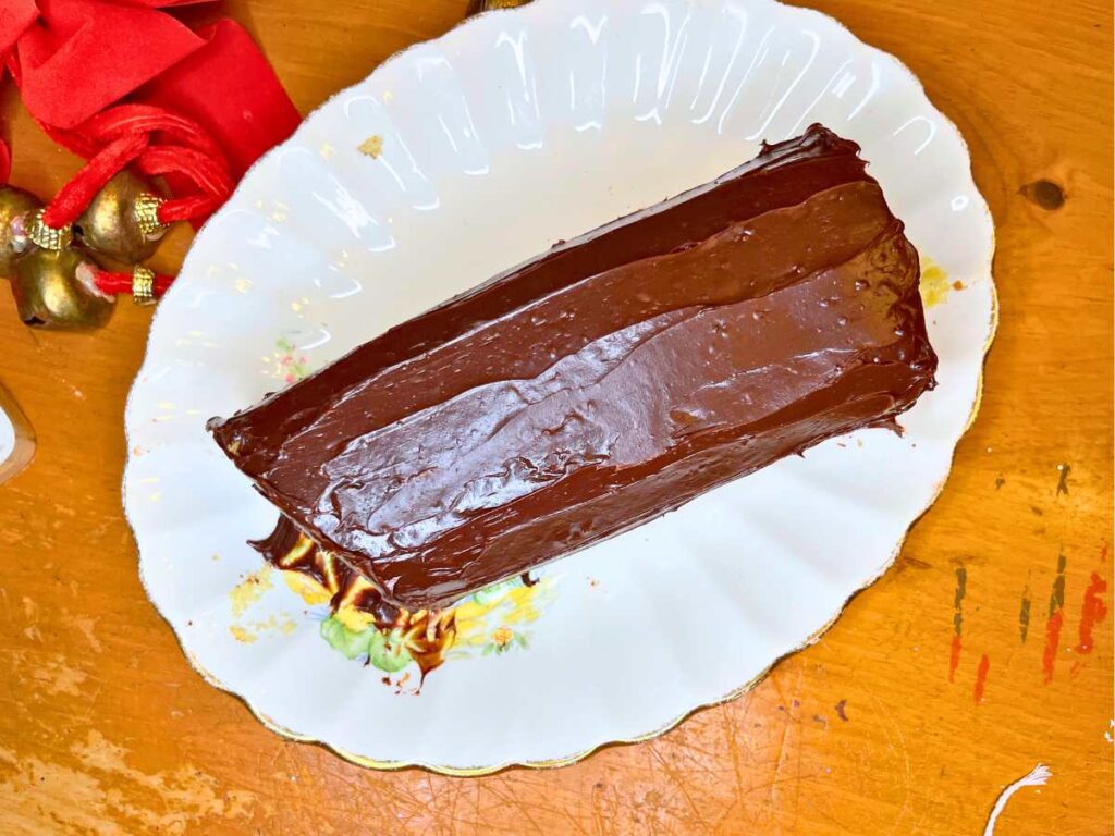 A cake in the shape of a log covered in chocolate ganache icing.