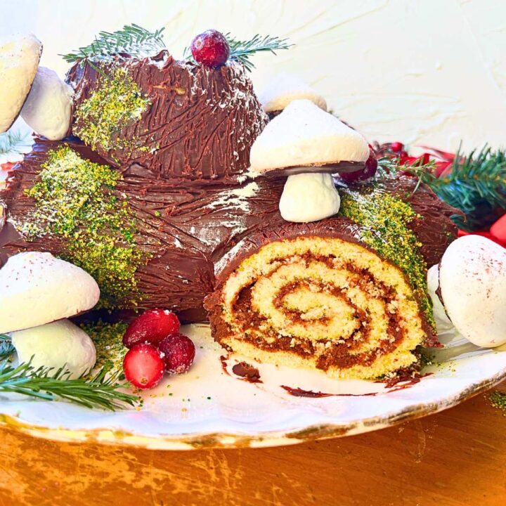 A yule log chocolate cake decorated with meringue mushrooms, cranberries, and evergreen pieces.