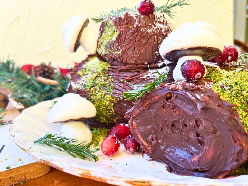 A jelly roll style cake in the shape of a log. Decorated with evergreen, meringue mushrooms, and cranberries.