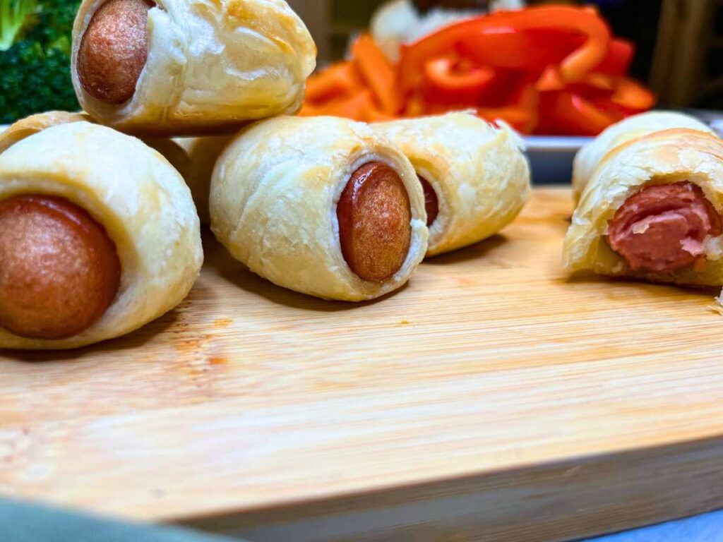 Small hotdogs wrapped in puff pastry on a wooden serving tray.