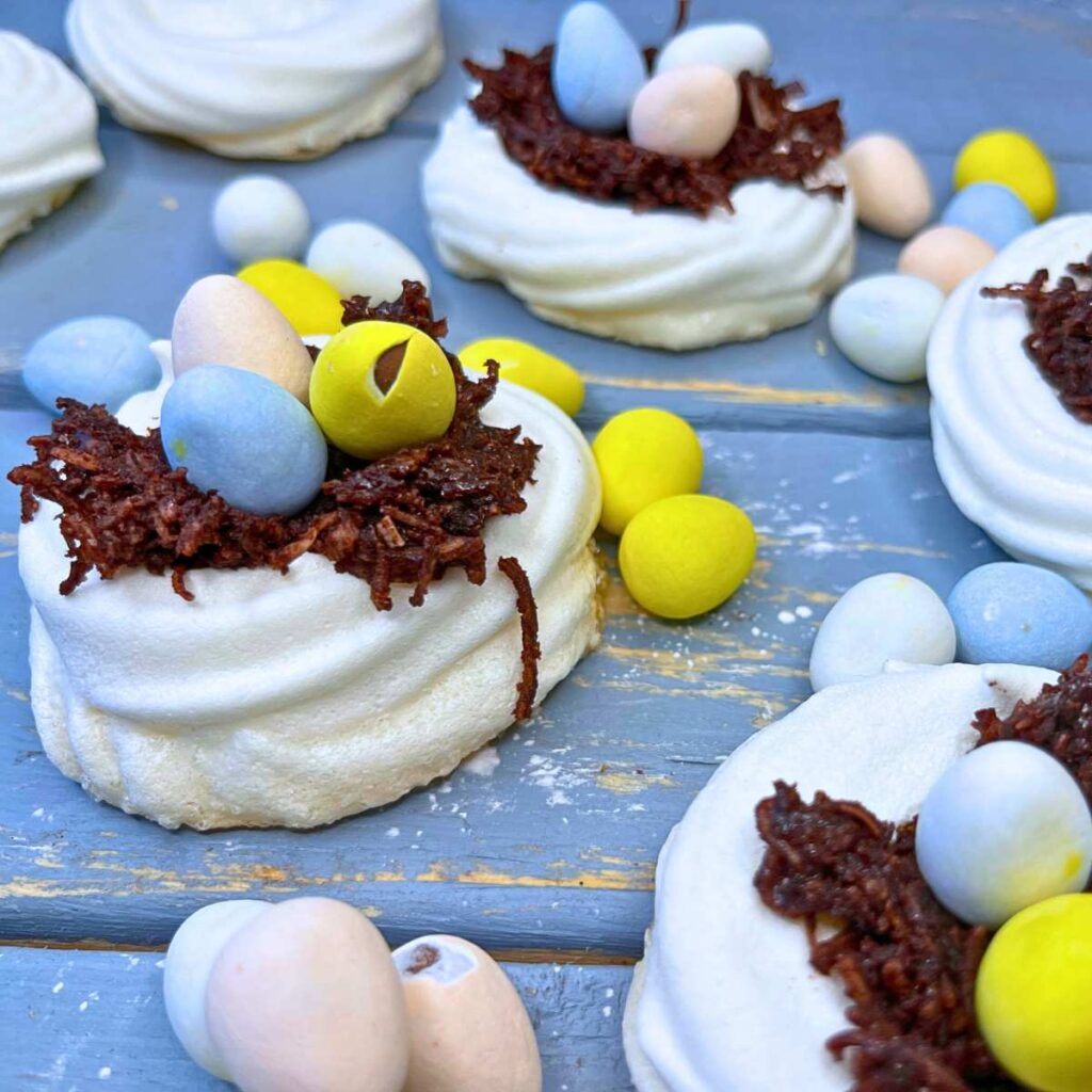 A group of meringue nests filled with chocolate and candy eggs.