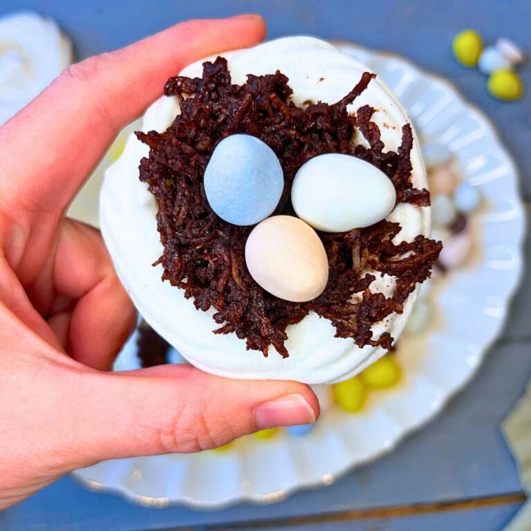 A woman is holding a meringue nest filled with chocolate and candy mini eggs.