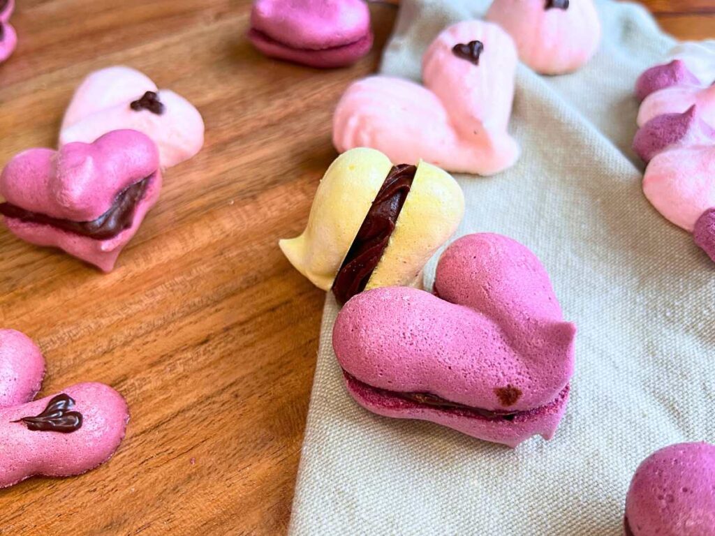 Some heart shaped meringue cookies that are sandwiched with chocolate ganache.