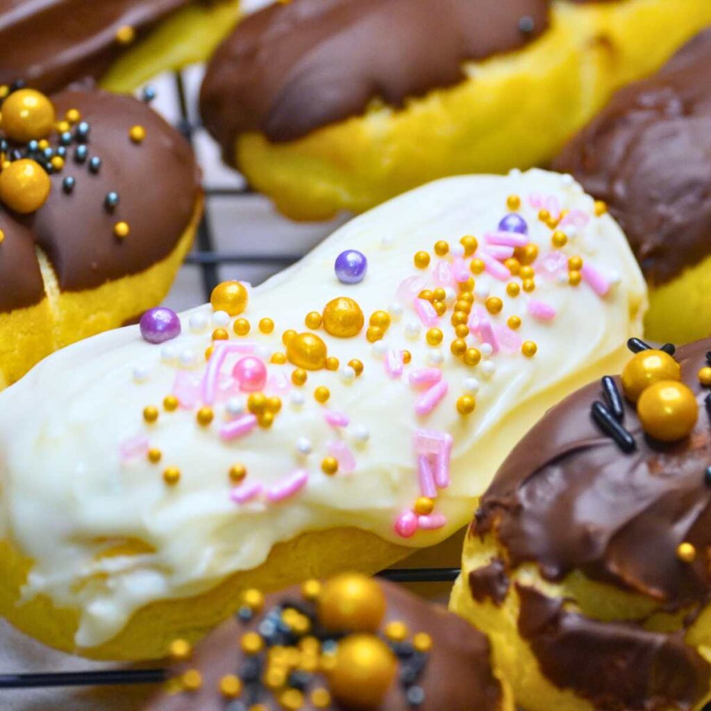 A group of chocolate dipped eclairs decorated with sprinkles. One is dipped in white chocolate.