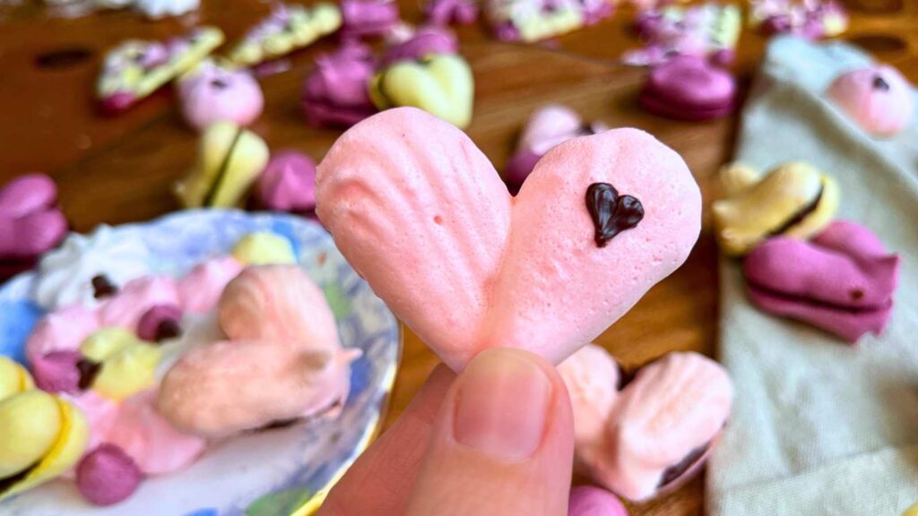 A woman is holding a heart meringue cookie decorated with a little chocolate heart.