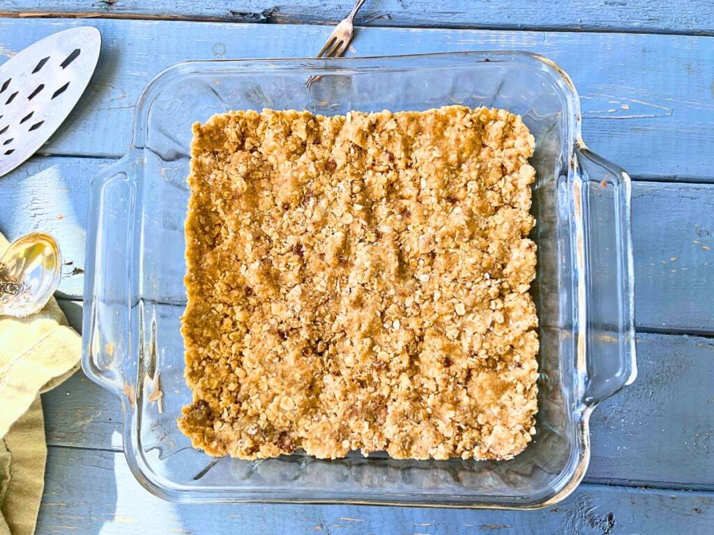 A glass square casserole dish with a crumble layer pressed inside.