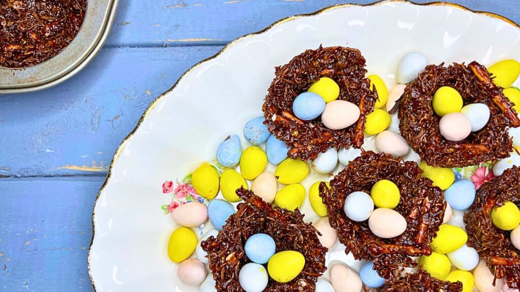 Chocolate nests on a white plate there are mini chocolate eggs around and inside of the nests.