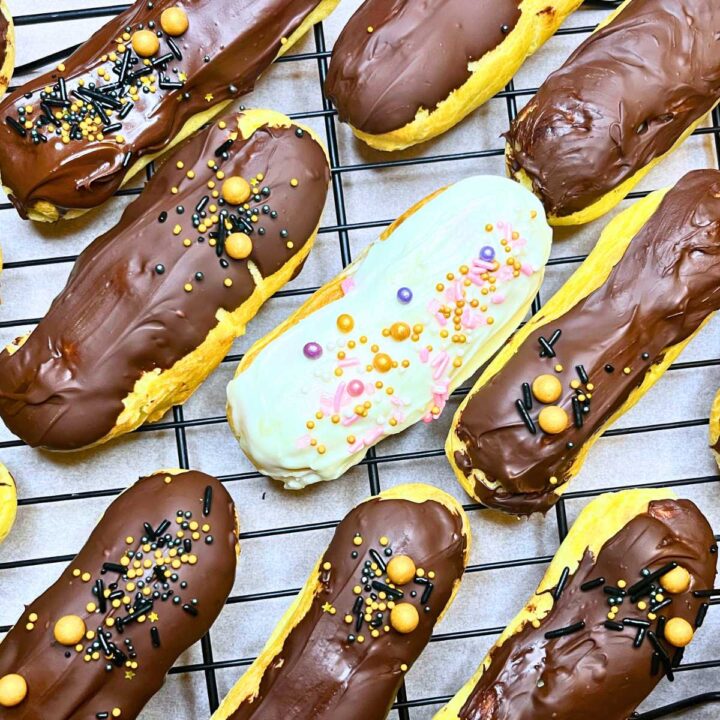 Some chocolate dipped eclairs on a wire rack. One is dipped in white chocolate and all have sprinkles.