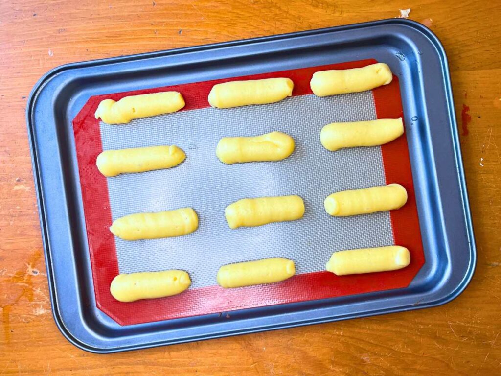 A lined baking sheet with lines of choux paste.