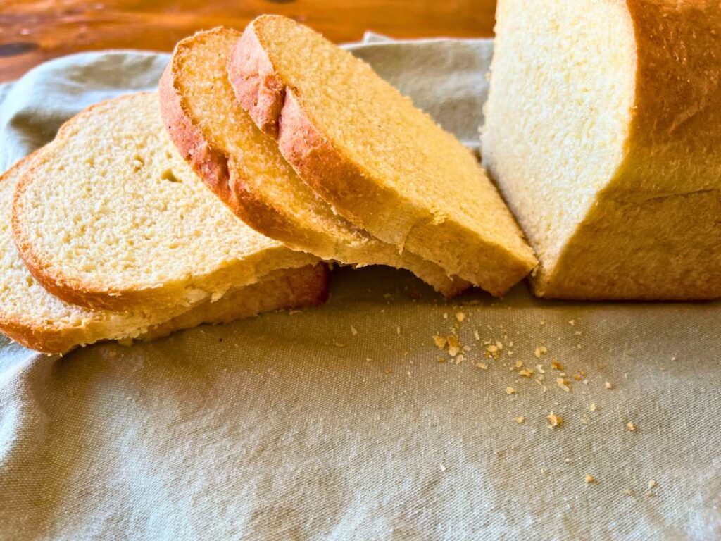 A sliced loaf of cornmeal white sandwich bread on a grey linen.