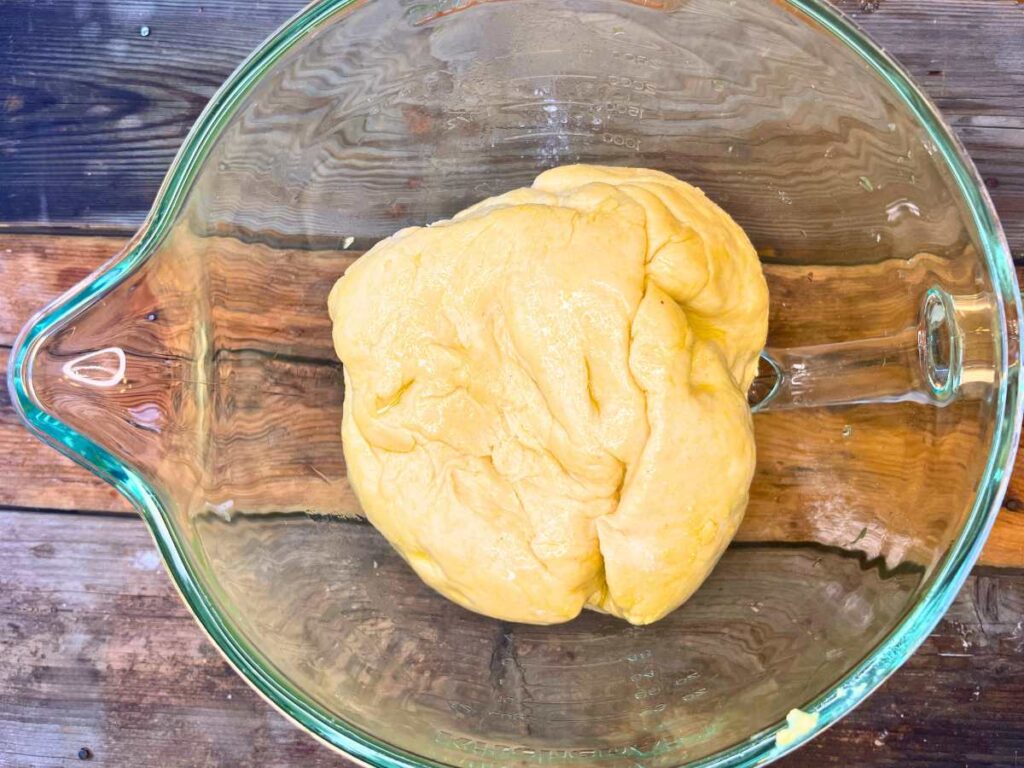 A glass bowl with cornmeal bread dough inside.