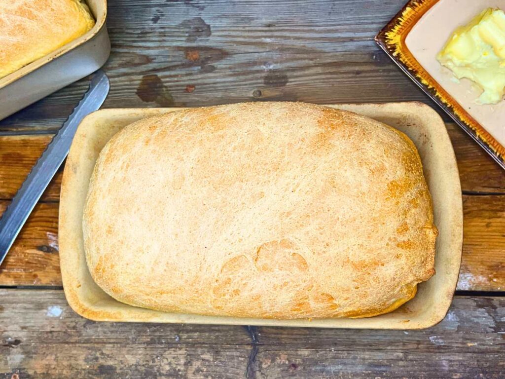 A baked loaf of cornmeal white sandwich bread in a stone loaf pan.