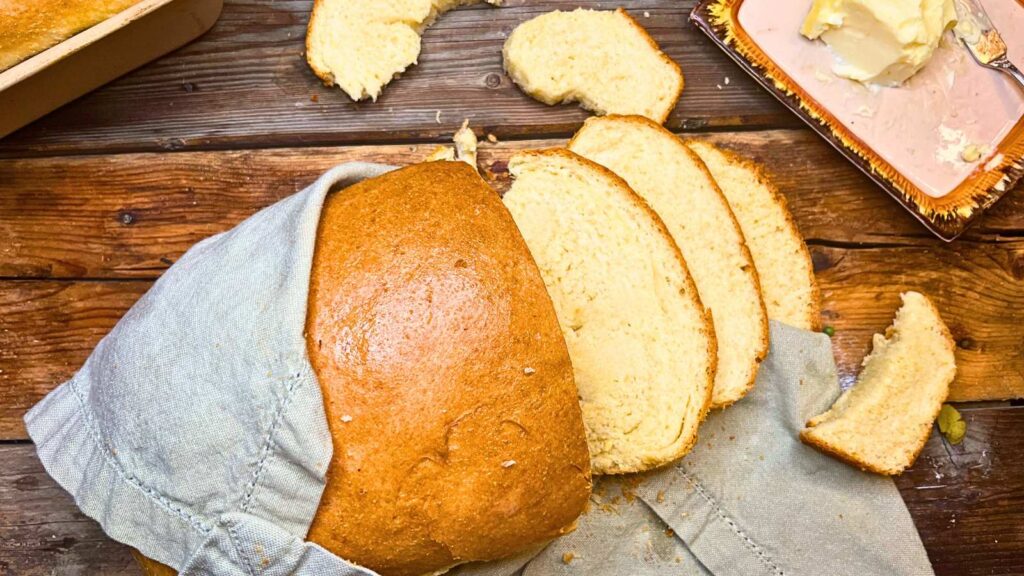 An overhead view of a loaf of sliced bread. There is a linen napkin over the loaf.