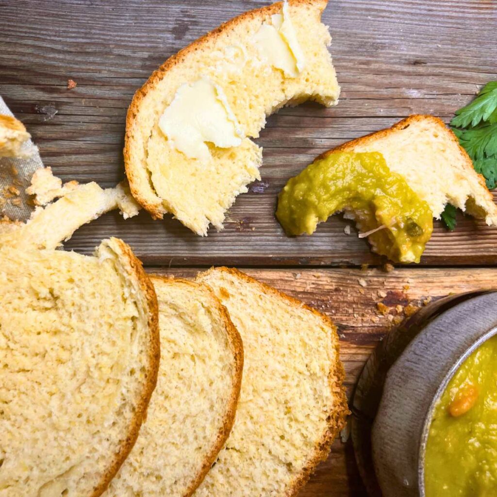 A sliced loaf of cornmeal bread on a wooden table. One has been dipped in soup.