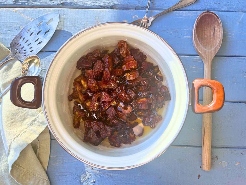 A white pot with chopped dates, water, lemon juice, and corn syrup inside.