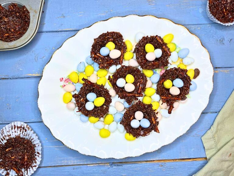 An overhead view of chocolate nests filled with mini candy eggs on a white plate.