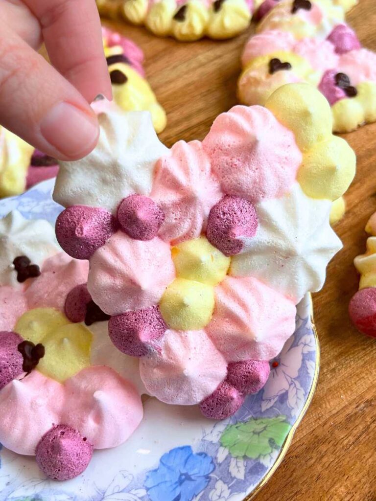 A woman is holding a large multicoloured meringue cookie. 