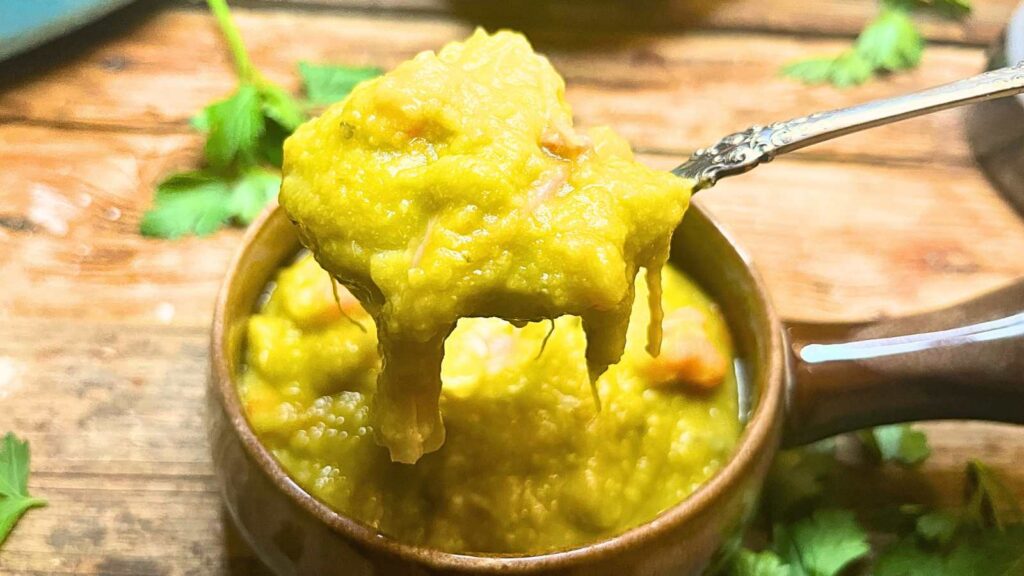 A woman holding up a spoonful of split-pea soup above a bowl of soup.